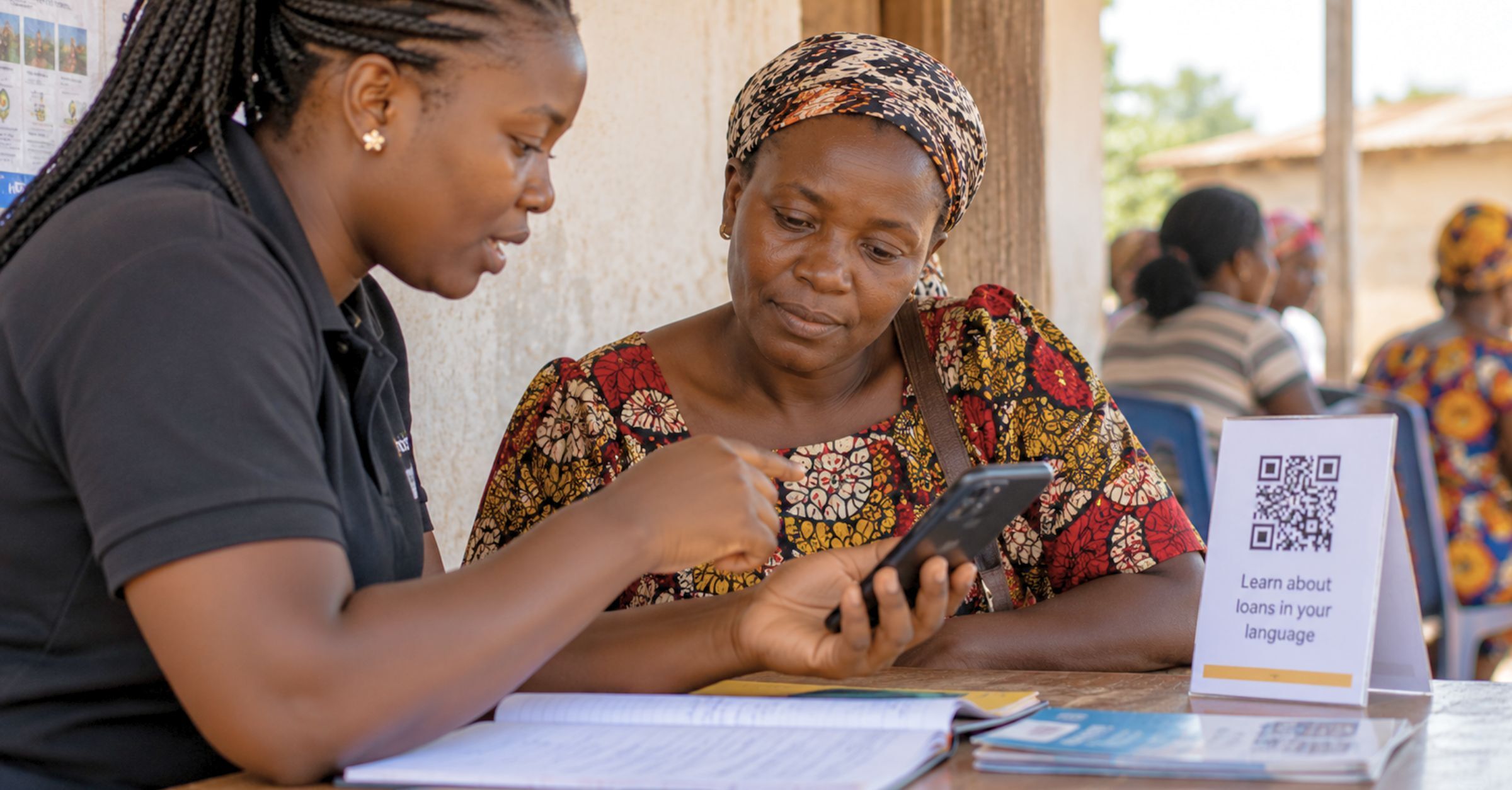 Two women in a village savings group listening to digital financial literacy education audio on their mobile phone.